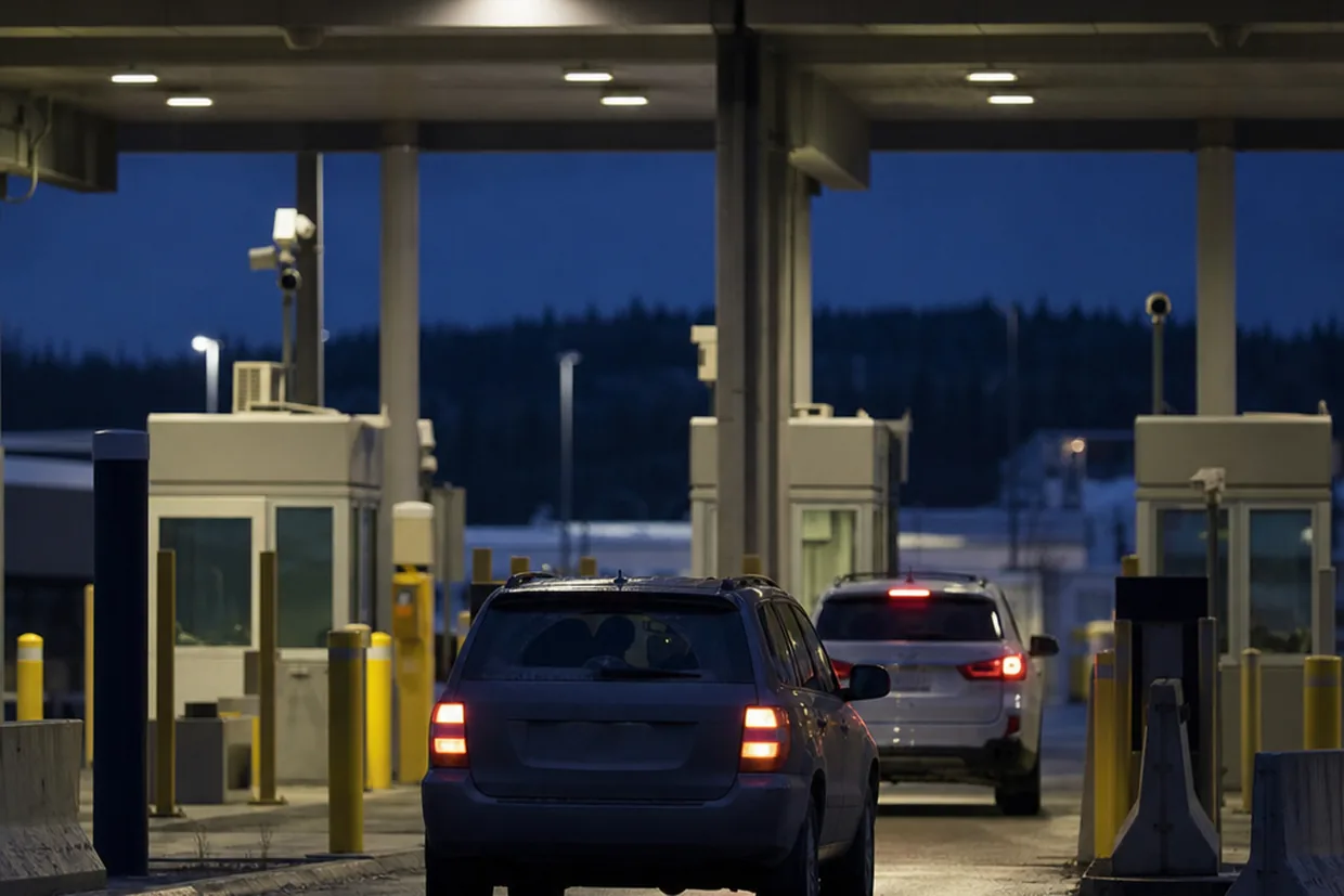 A single lane of traffic queued at a Canadian land border crossing at dusk, documentary and unglamorous