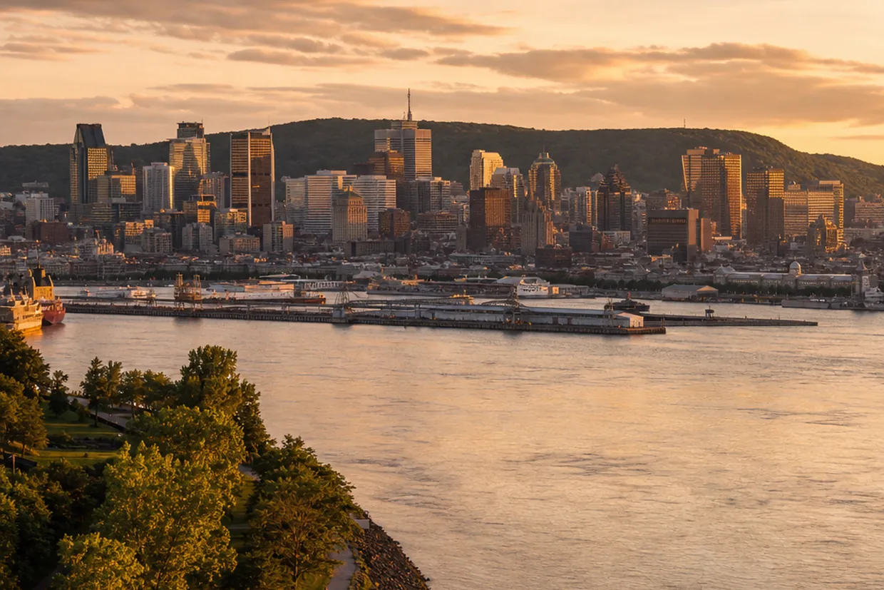Montreal's downtown skyline rises above the St. Lawrence River at golden hour, seen from the water's edge.