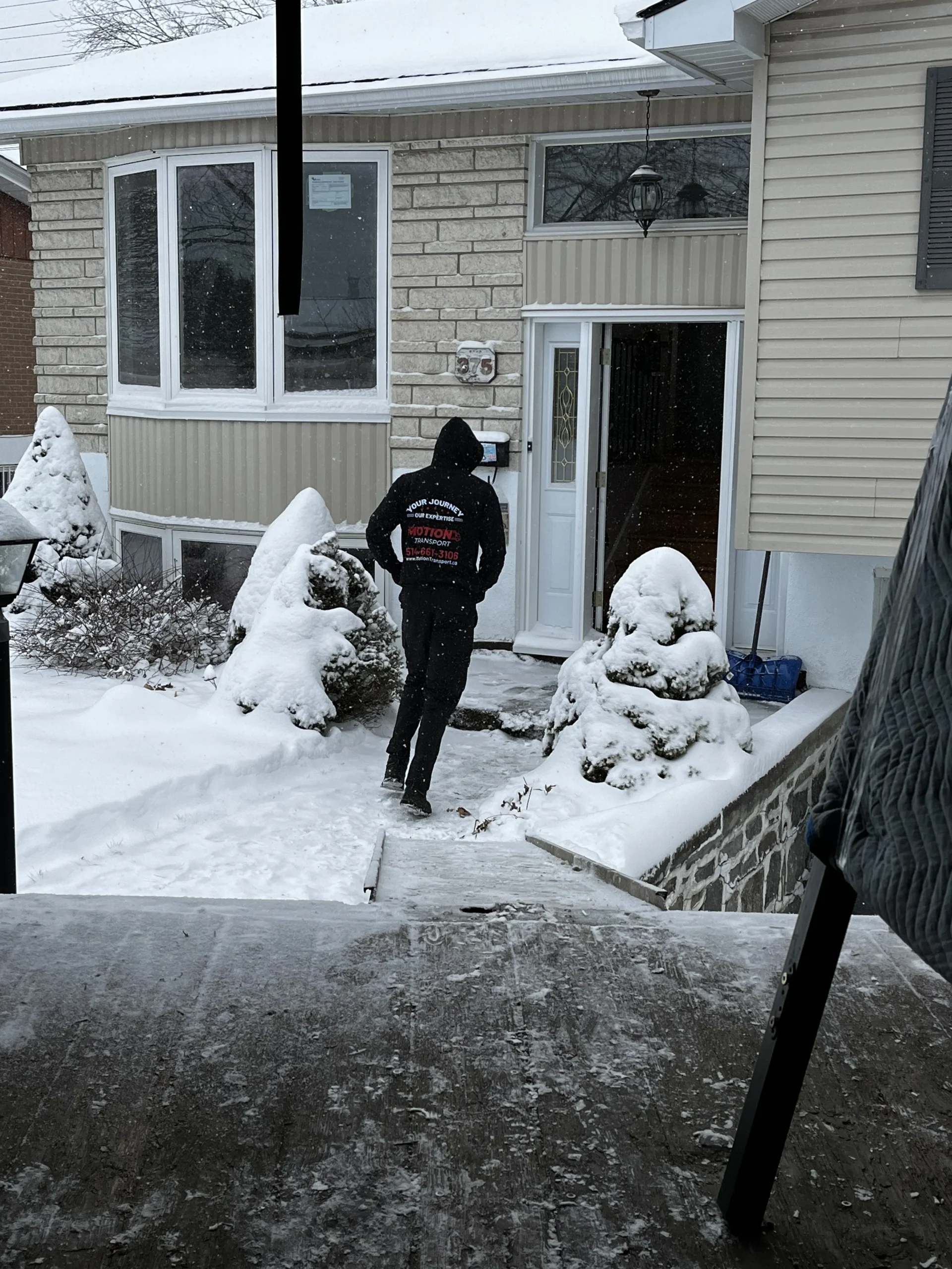 A Motion Transport team member in a branded jacket walking up snowy front steps to a customer's home